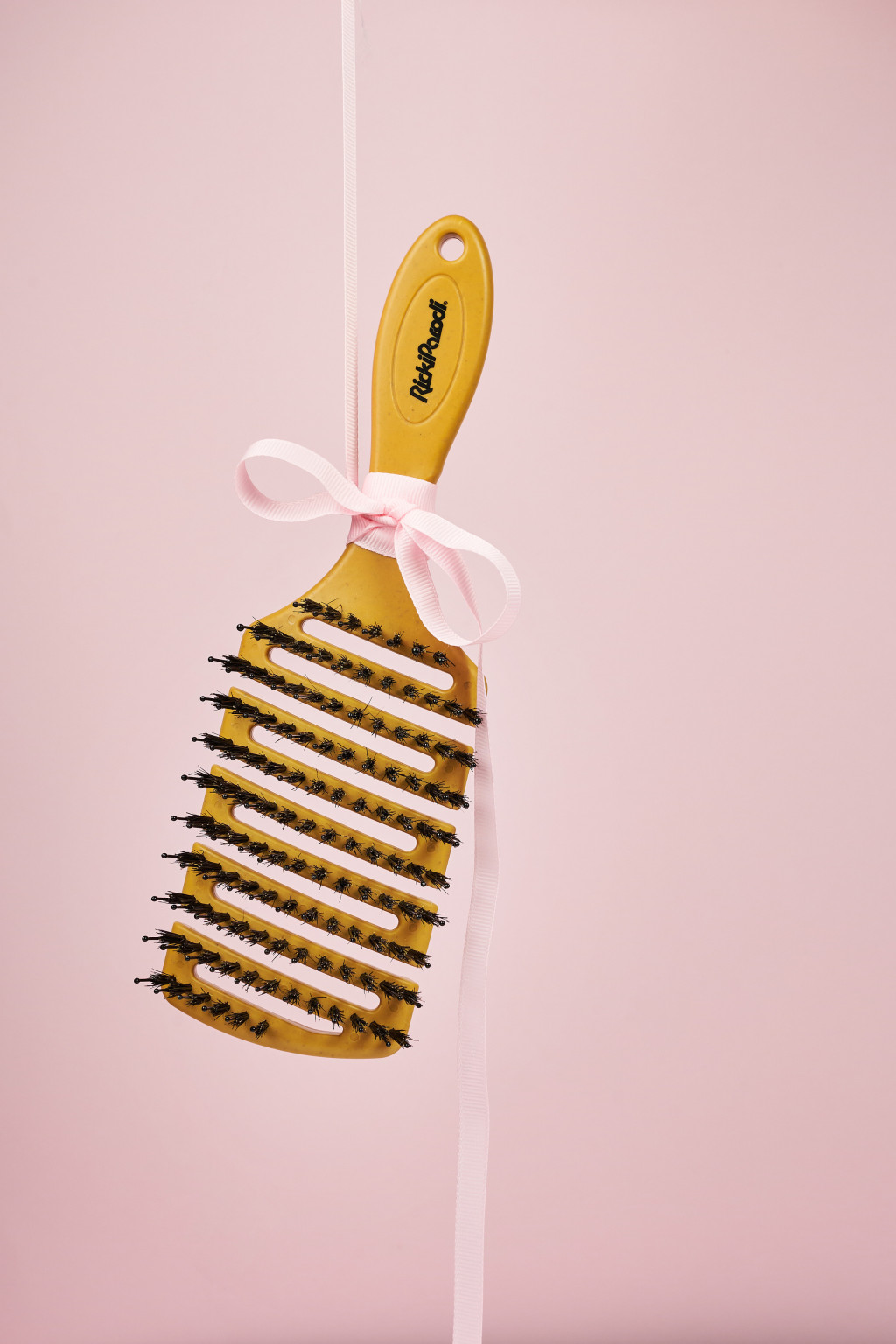 Escova de cabelo amarela com cerdas pretas e fita rosa pendurada