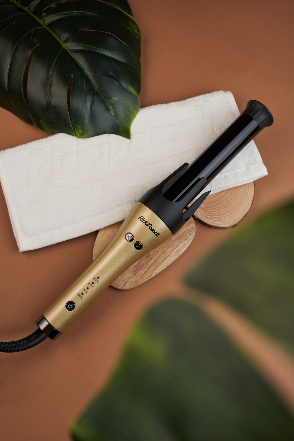 Modelador de cabelo automático dourado e preto com botões e toalha branca em fundo castanho