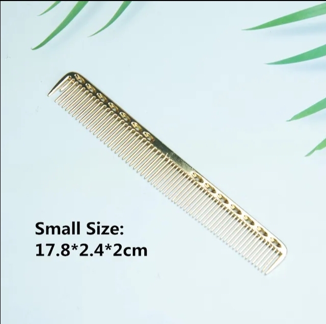 Pente pequeno dourado com padrão, sobre superfície branca com folhas verdes