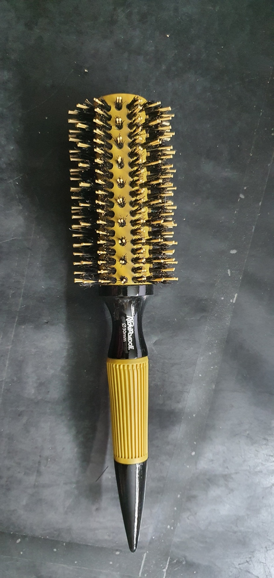 Escova de cabelo redonda com cerdas e cabo preto e amarelo sobre superfície cinza