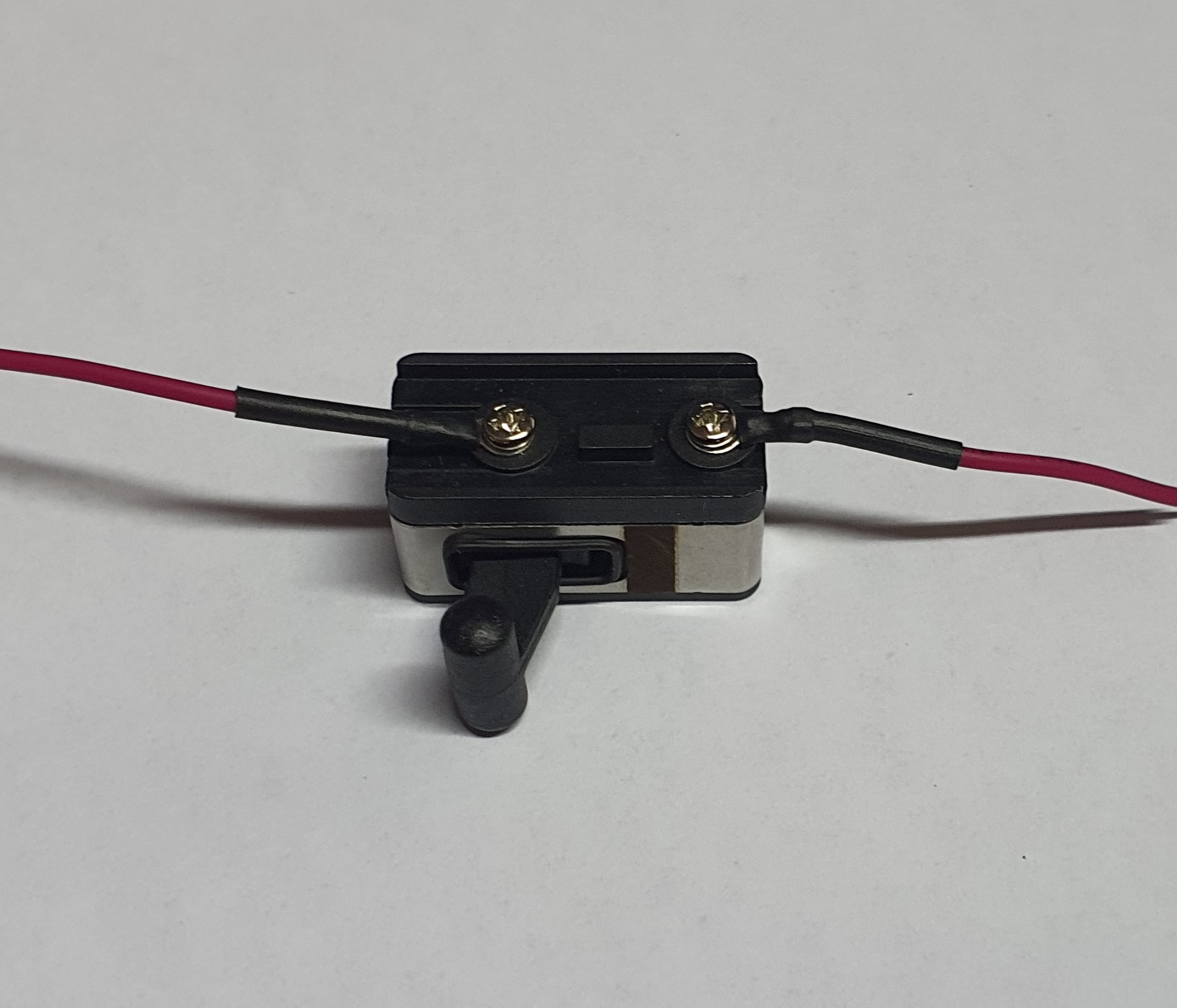 Interruptor de alavanca preto com cabos vermelhos numa superfície branca