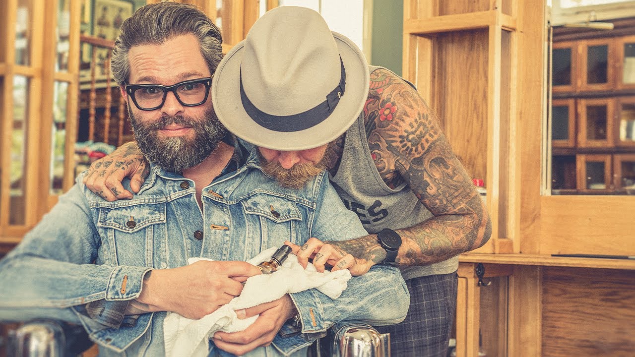 Dois homens seguram e acariciam um pequeno animal num ambiente interior com decoração em madeira.
