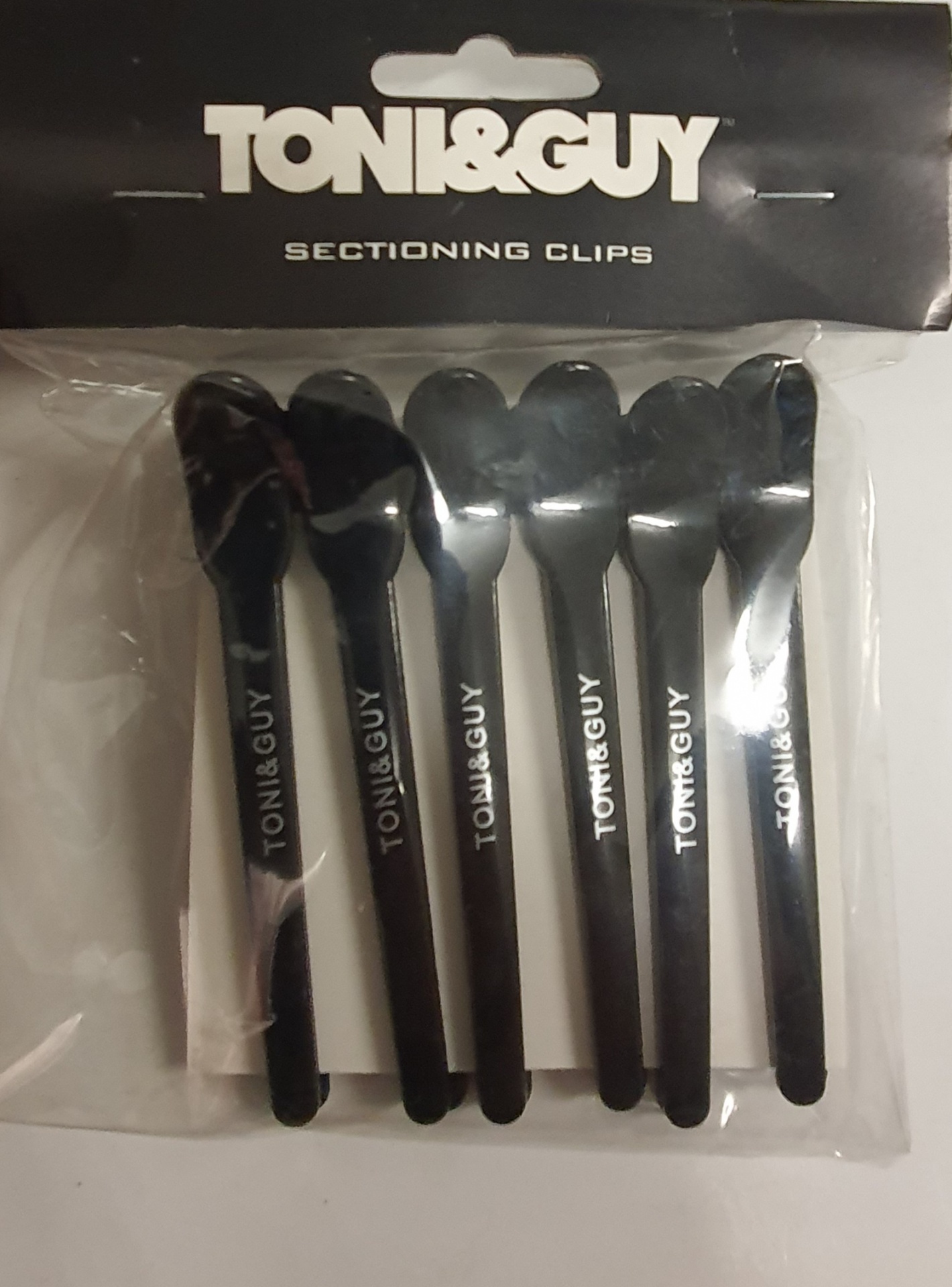 Cinco ganchos de secção pretos TONI&GUY em embalagem plástica com cartaz preto