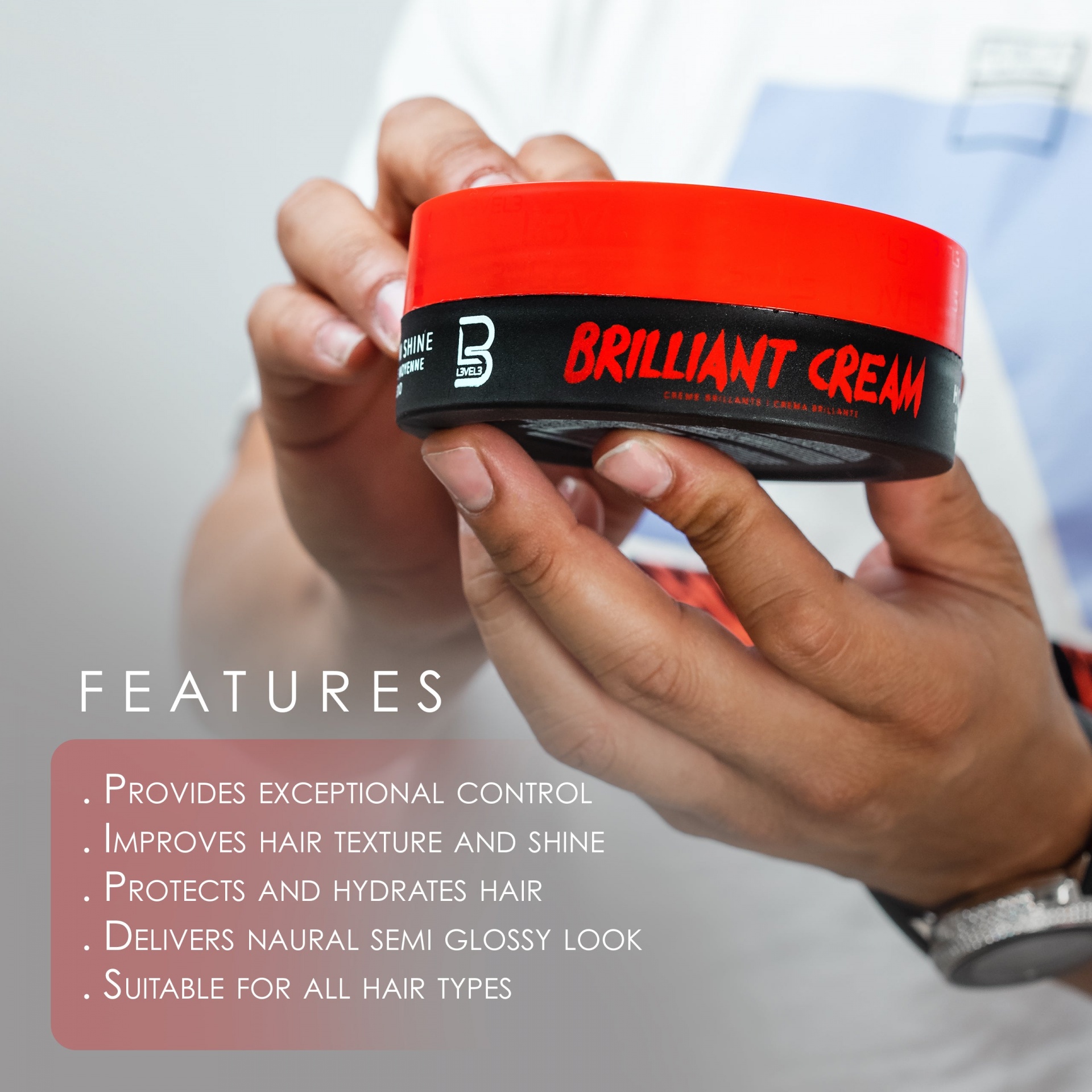 Frasco de creme para cabelo BRILLIANT CREAM com tampa vermelha e corpo preto, segurado por mãos.