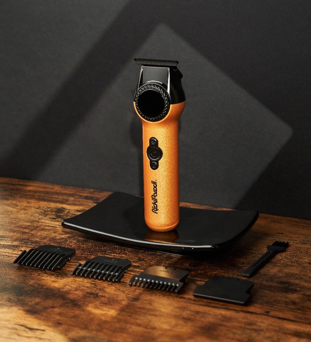 Máquina de corte cabelo preta e dourada com acessórios sobre mesa de madeira