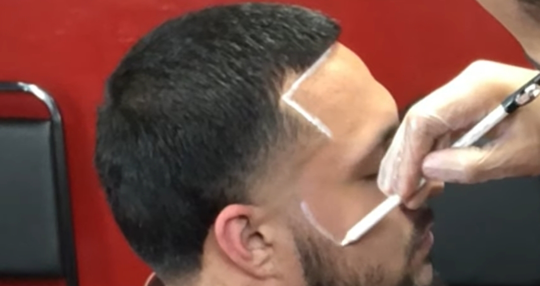 Homem com cabelo curto e barba a receber desenho com giz branco na testa e face