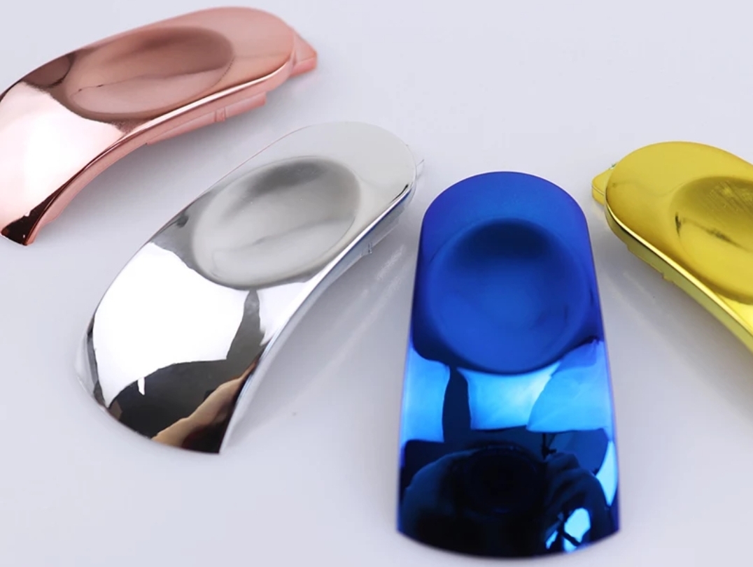 Peças metálicas coloridas com acabamento espelhado sobre superfície branca