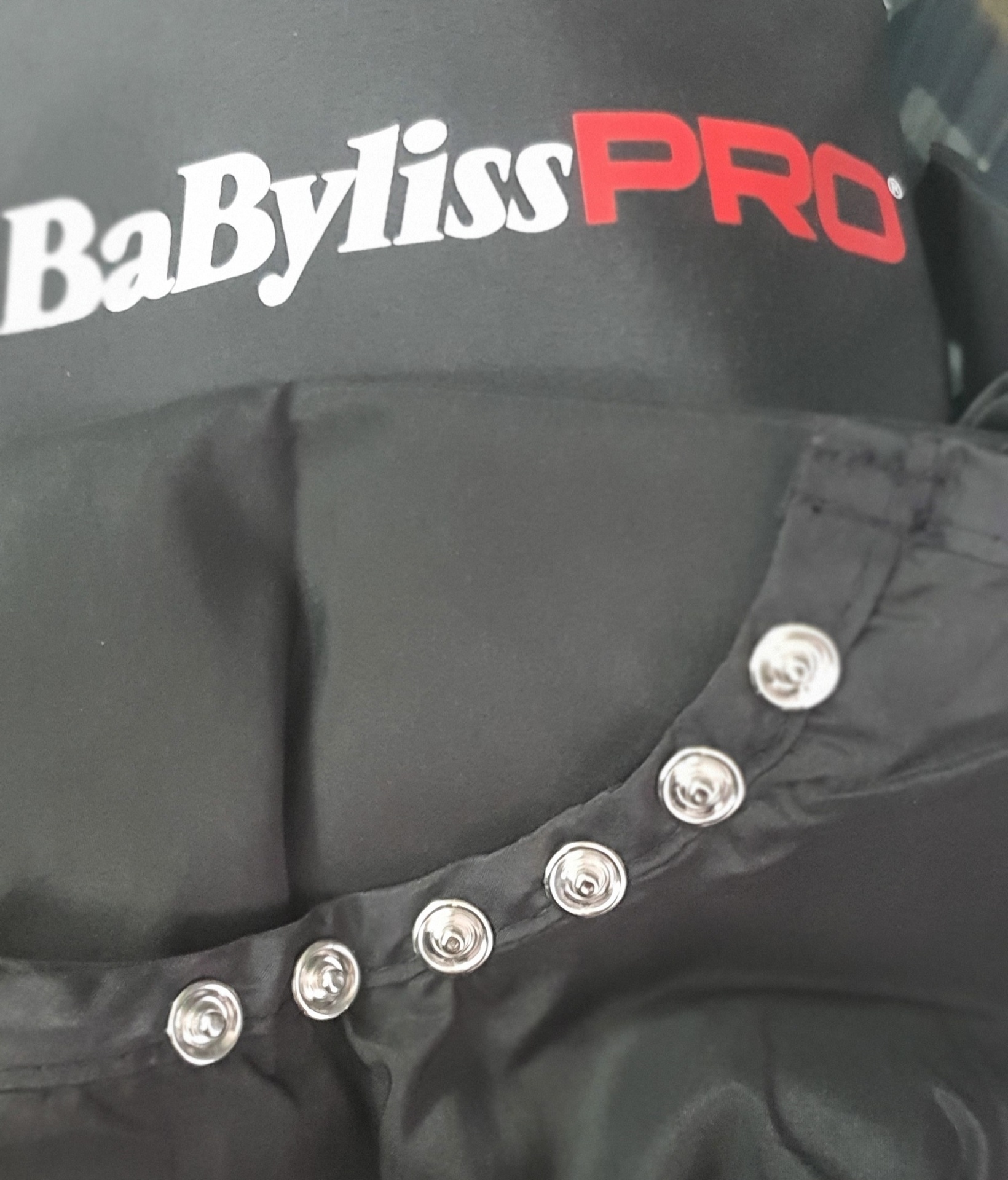 Tecido preto com botões de pressão e logo BaBylissPRO