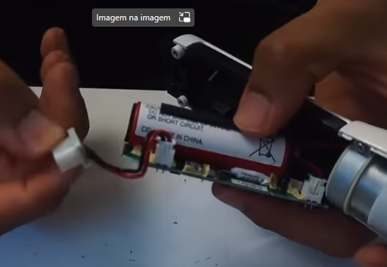 Dispositivo eletrónico desmontado com fios e bateria expostos e mãos a manipular os componentes