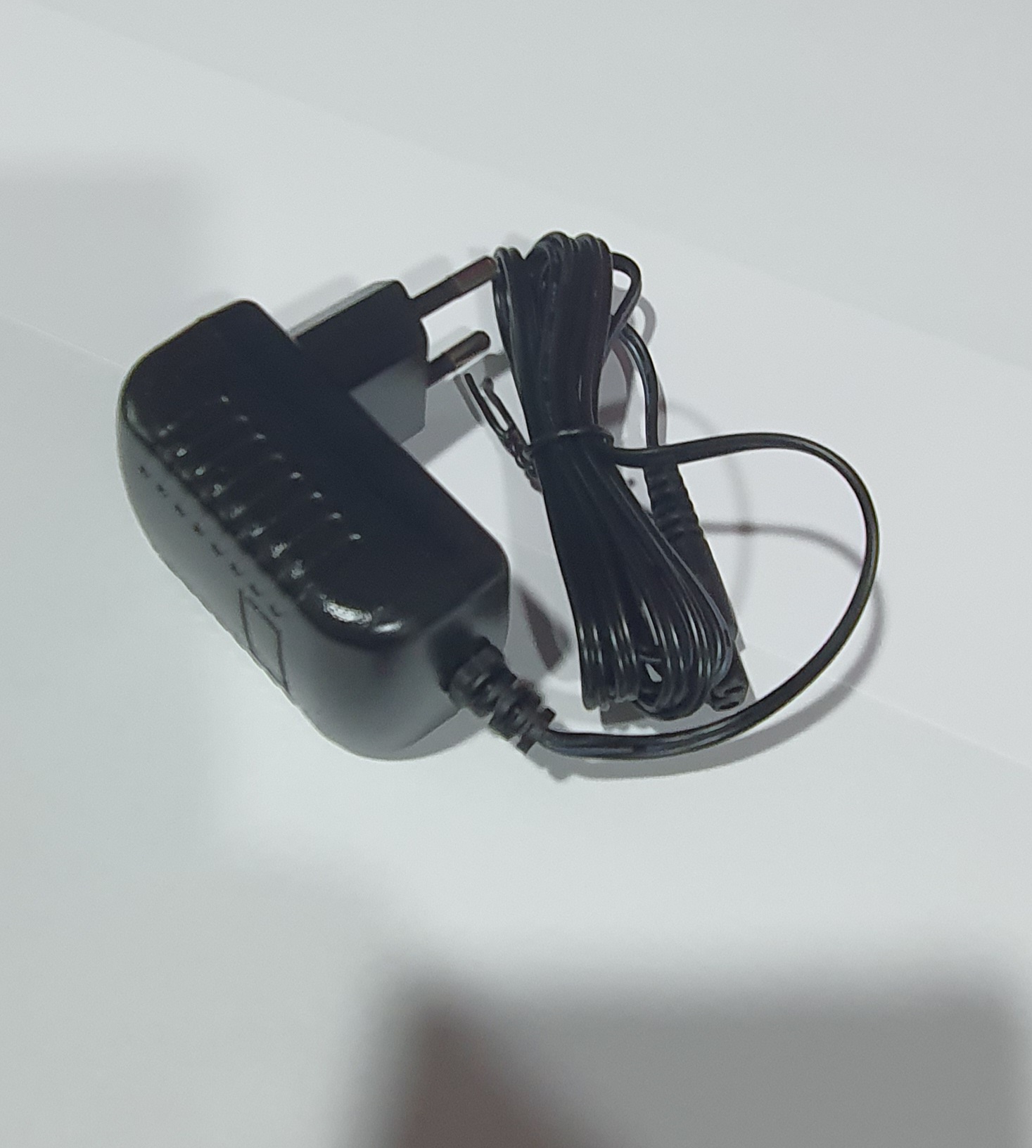 Carregador de parede preto com cabo enrolado sobre superfície branca