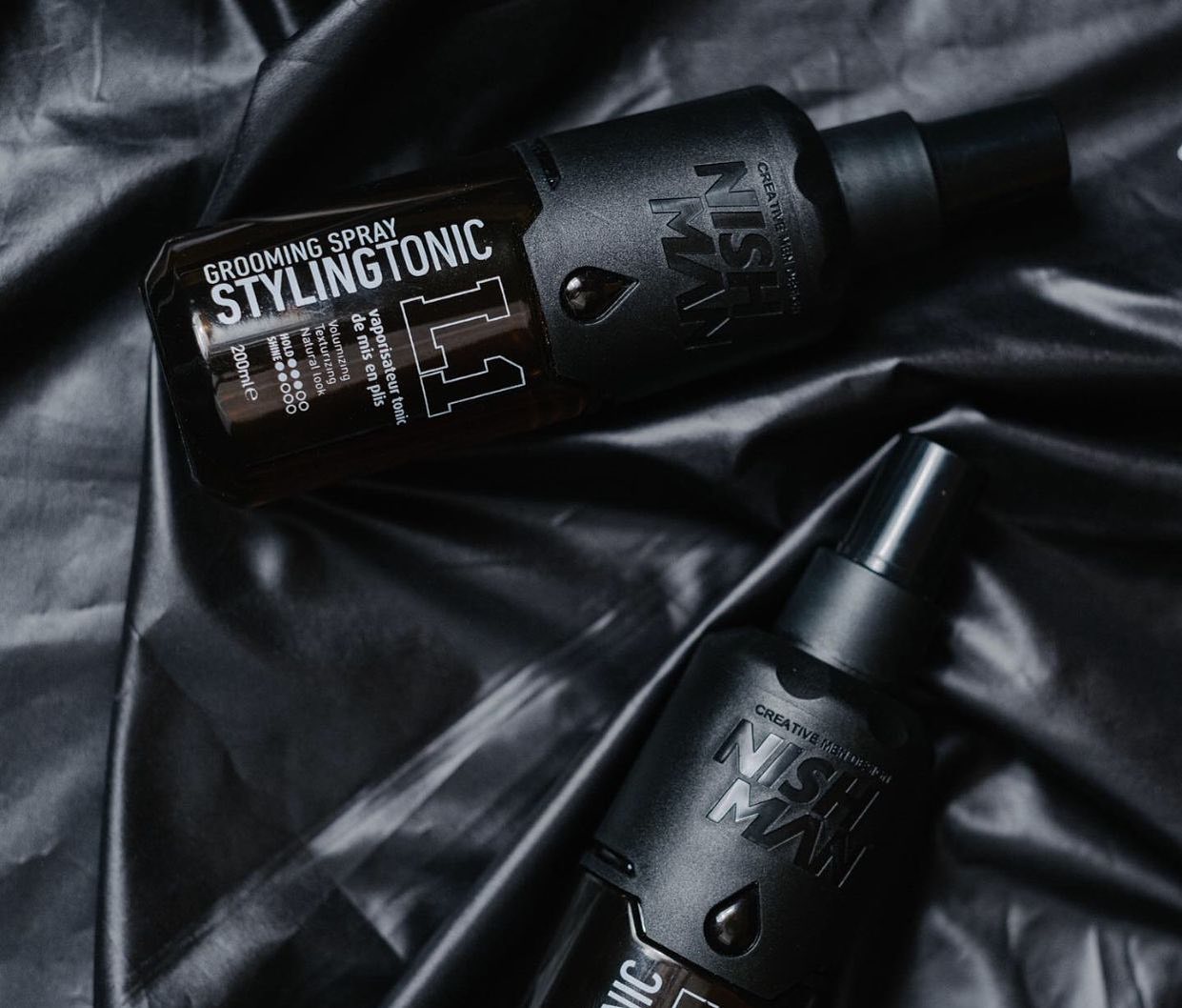 Frascos pretos de spray de cabelo Styltgtonic sobre tecido preto brilhante.
