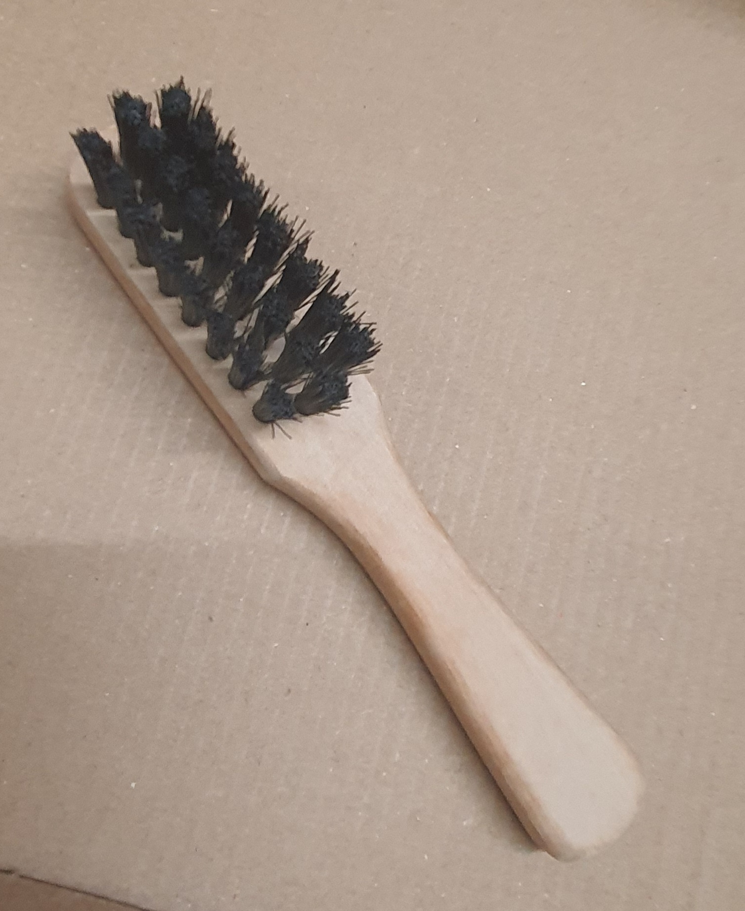 Escova de madeira com cerdas pretas sobre superfície castanha clara