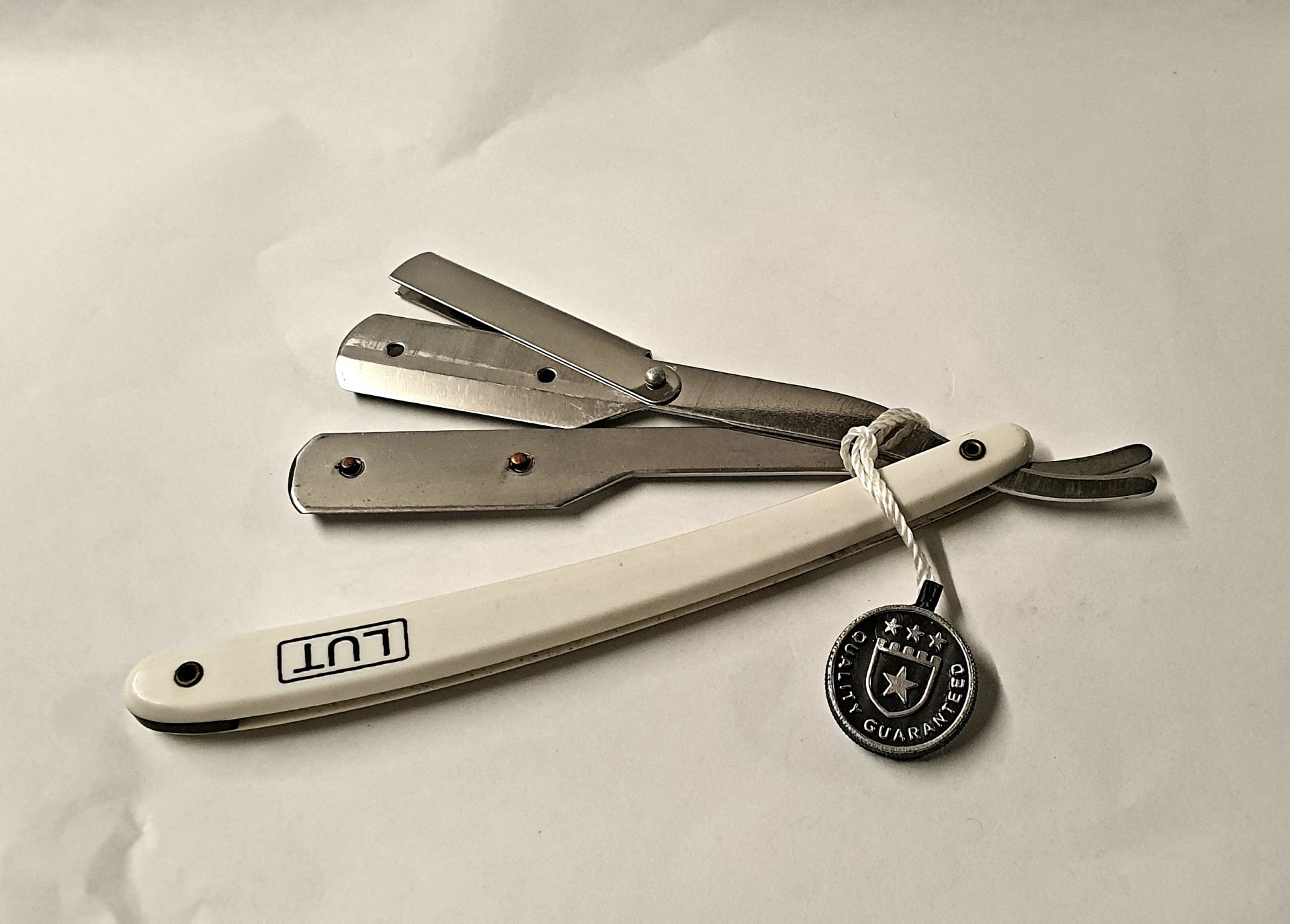 Navalha de barbear reta com cabo branco e lâmina em aço, etiqueta preta com estrela.