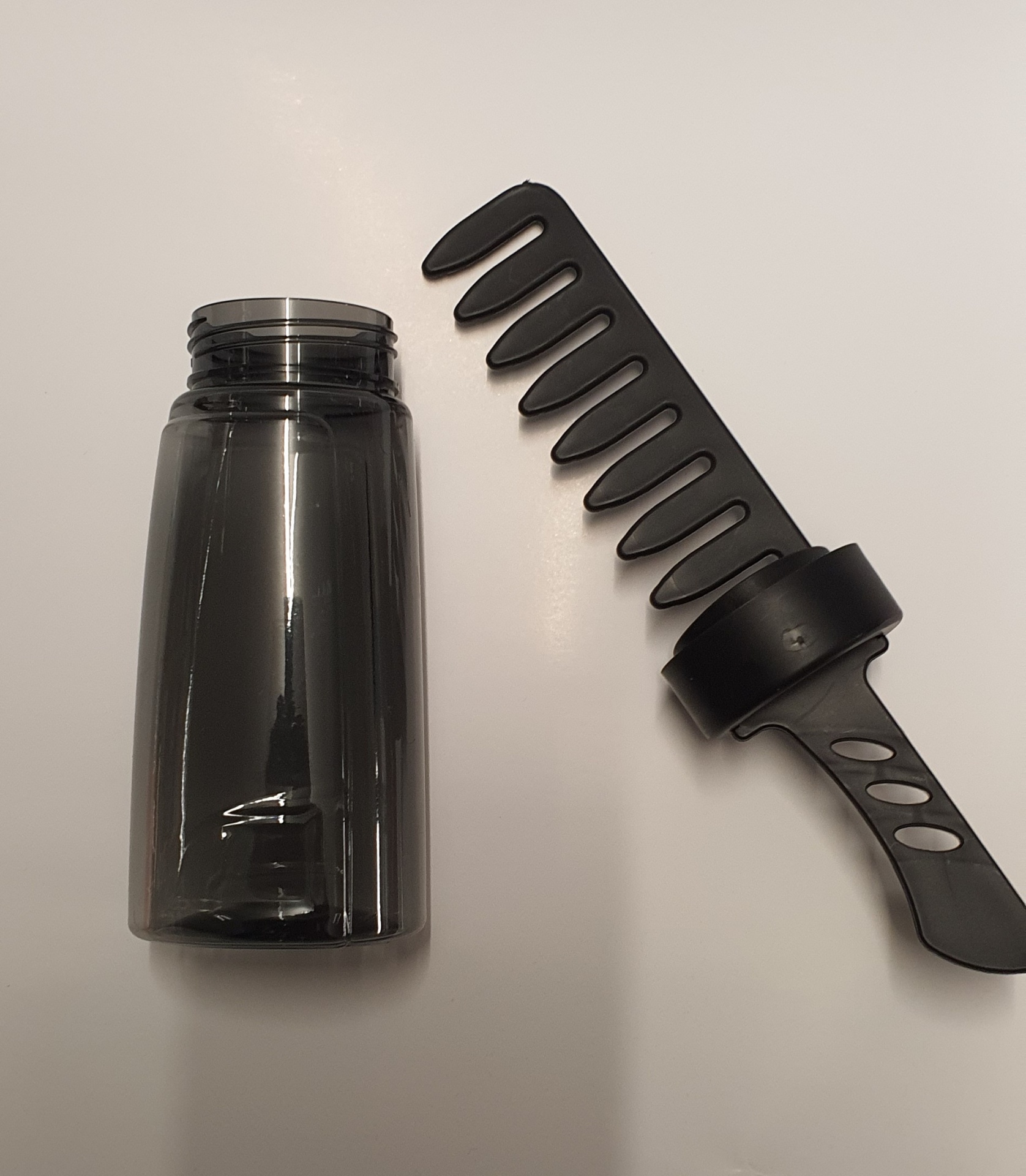 Frasco transparente fumado e pente largo preto sobre fundo branco