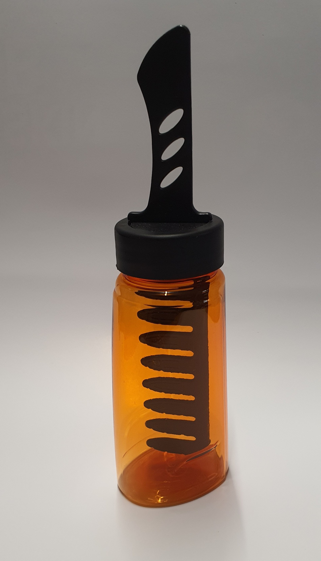 Frasco plástico âmbar com tampa preta e peça preta com recortes.
