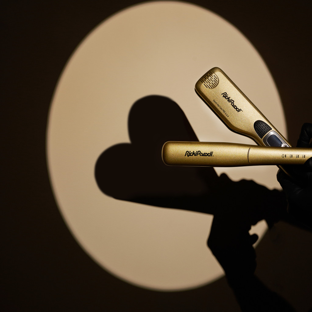 Prancha dourada para cabelo com marca Rich Pearl segurada com luva preta e sombra em fundo iluminado