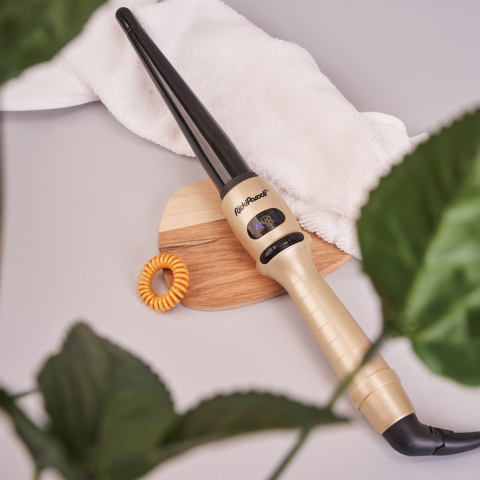 Modelador de cabelo dourado com visor digital sobre base de madeira e toalha branca