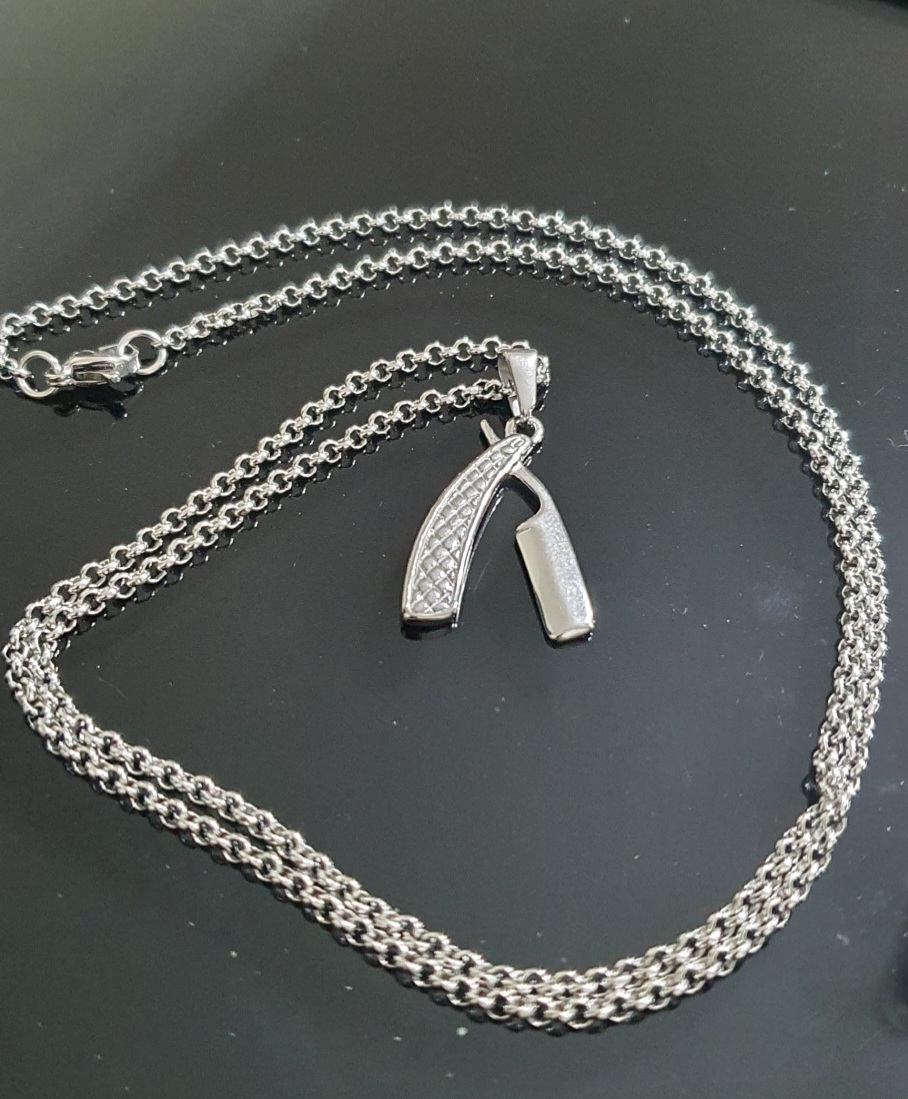 Colar prateado com pendente de navalha sobre superfície preta