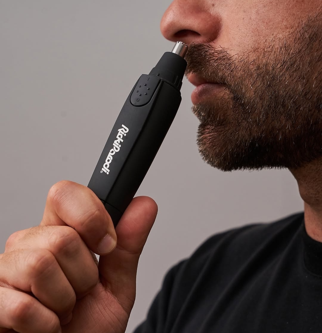 Aparelho negro para aparar pêlos do nariz em uso próximo ao rosto de um homem com barba.