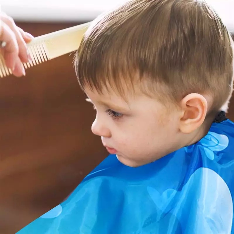 Criança a ser penteada com capa azul em ambiente interno