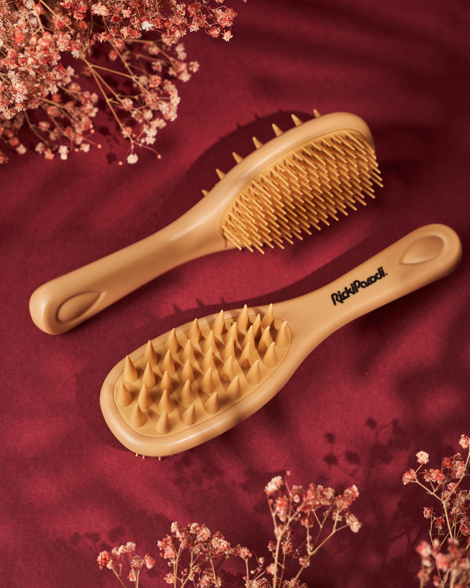 Duas escovas de cabelo cor de areia sobre tecido vermelho com flores secas