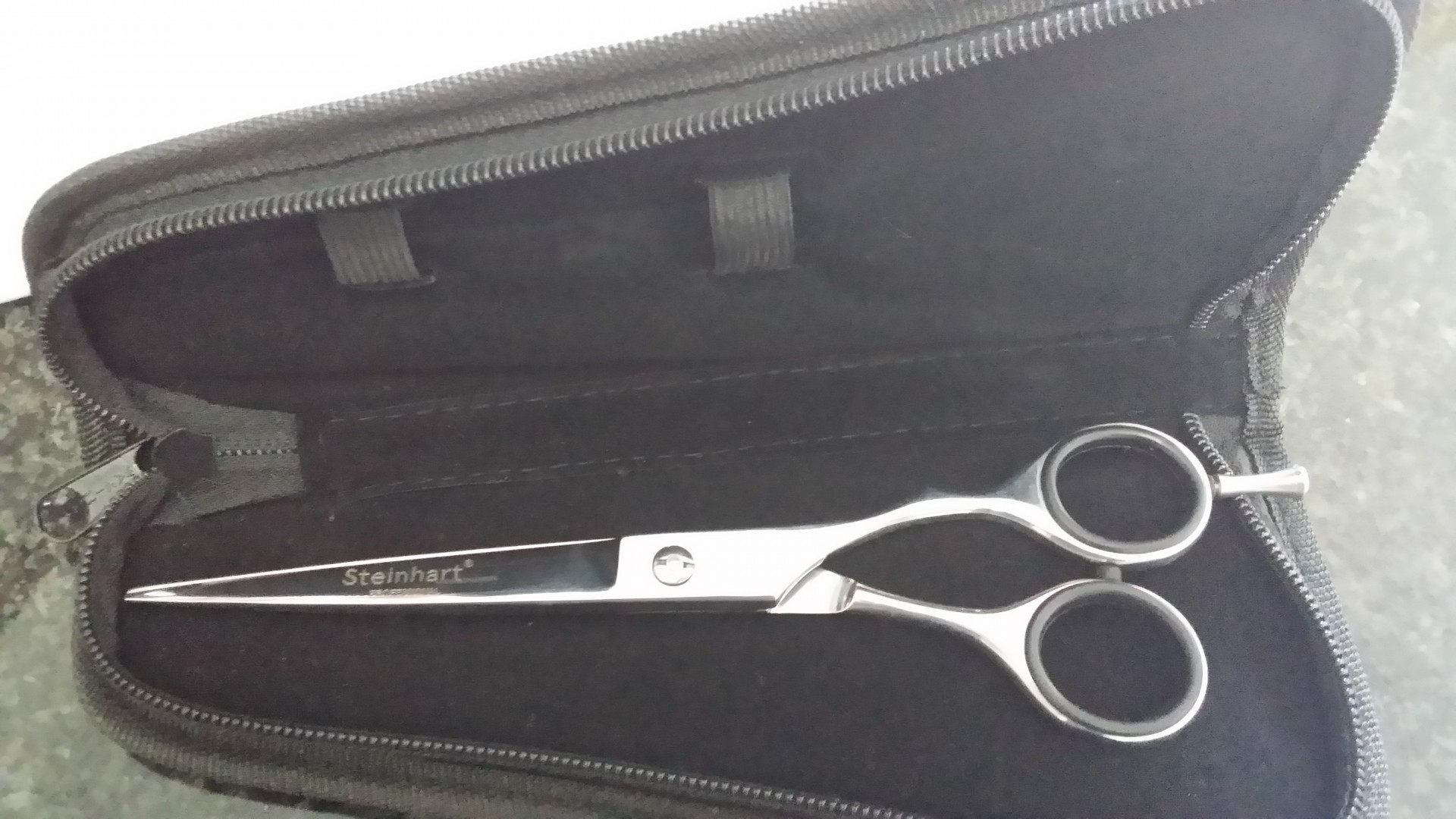 Tesoura de corte prateada com cabos pretos dentro de estojo preto