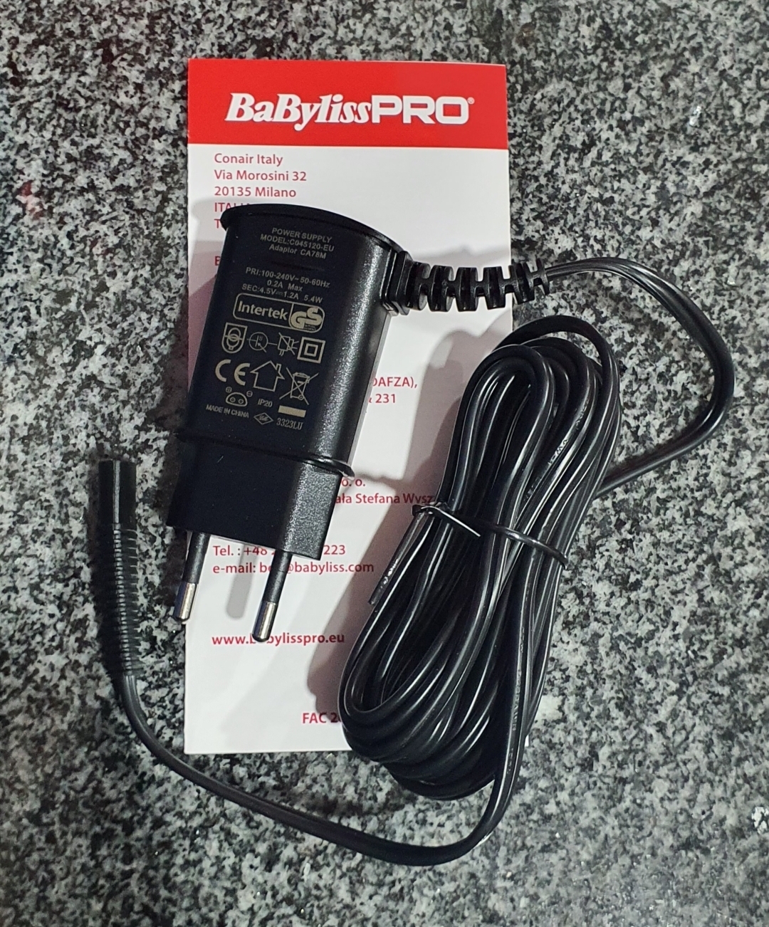 Carregador preto BaBylissPRO com ficha europeia sobre papel com logotipo vermelho e granito cinza.