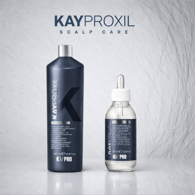 Frascos de produtos Kayproxil para cuidado do couro cabeludo em fundo cinza com textura de fios de cabelo