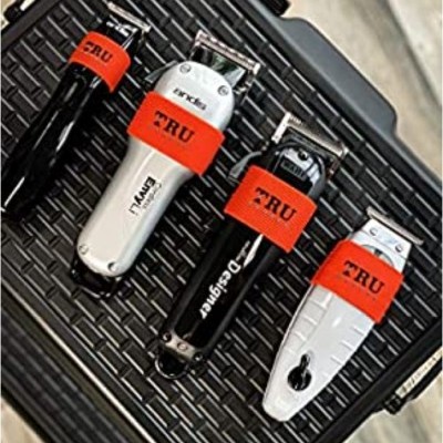 Quatro máquinas de cortar cabelo preta e branca com etiquetas vermelhas TRU sobre superfície preta texturizada.