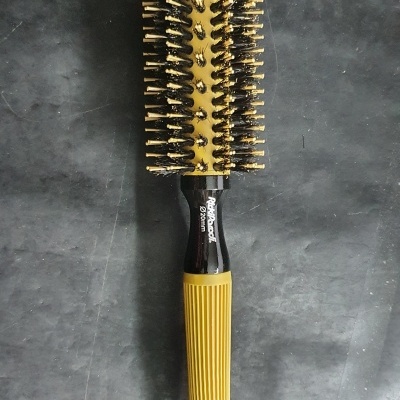 Escova de cabelo redonda com cerdas pretas e douradas e cabo preto e amarelo sobre superfície escura