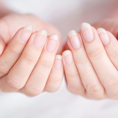 Mãos femininas com unhas naturais e cuidadas em fundo neutro.