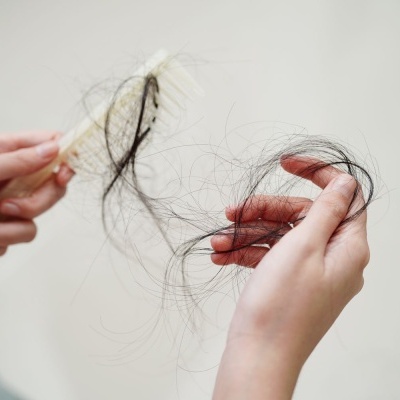 Mãos a segurar cabelo caído de uma escova de cabelo de madeira