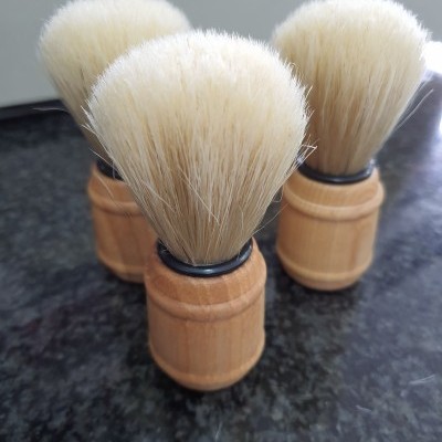 Três pincéis de barbear com cabos de madeira e cerdas brancas sobre superfície escura