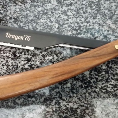 Barbeador naval preto com cabo de madeira castanha e proteção vermelha sobre granito cinza