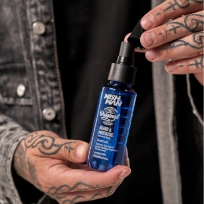 Frasco azul NISHMAN Beard & Mustache em mãos tatuadas