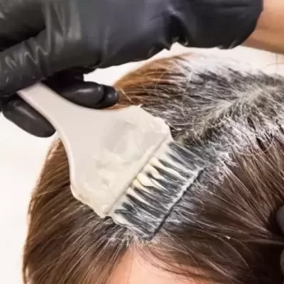 Aplicação de tinta castanha na raiz do cabelo com pincel e luvas pretas