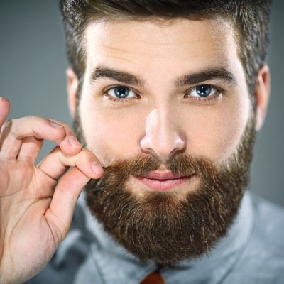 Homem com barba castanha espessa a segurar bigode e camisa cinza