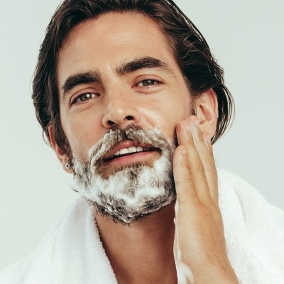 Homem a fazer a barba com espuma branca e toalha ao redor do pescoço