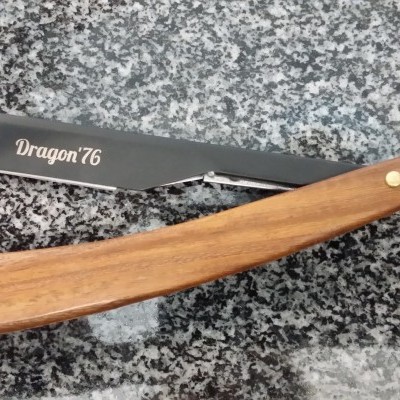 Navalha de barbear com lâmina preta e cabo de madeira clara sobre granito cinzento