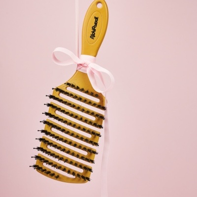 Escova de cabelo amarela com cerdas pretas e fita rosa pendurada
