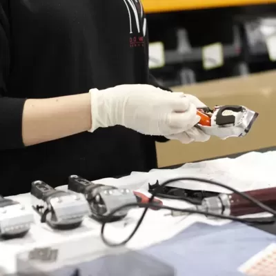 Pessoa com luva branca segurando máquina de cortar cabelo sobre mesa com outras máquinas e acessórios