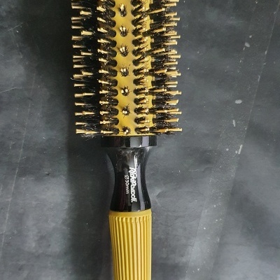 Escova de cabelo redonda com cerdas e cabo preto e amarelo sobre superfície cinza