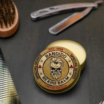 Pote de bálsamo para barba Bandido com arte de caveira em tampa, navalha, escova e pente ao fundo