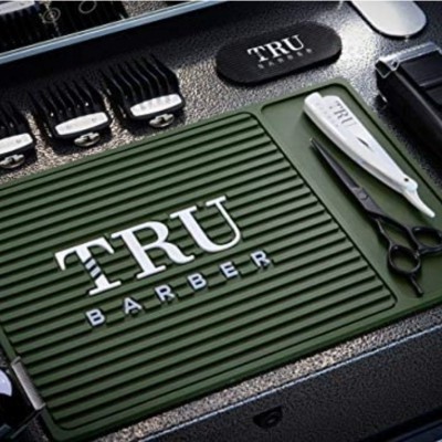 Conjunto de utensílios de barbeiro com base verde TRU BARBER, navalha branca, tesoura preta e acessórios sobre superfície preta.
