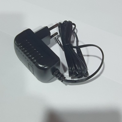 Carregador de parede preto com cabo enrolado sobre superfície branca