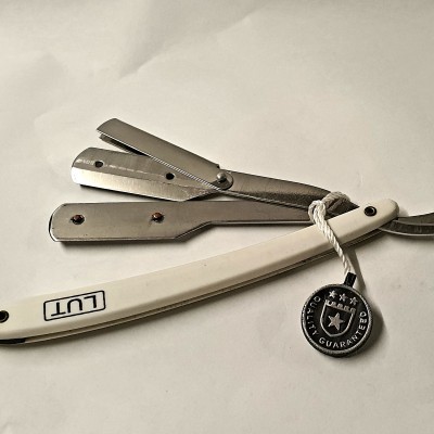 Navalha de barbear reta com cabo branco e lâmina em aço, etiqueta preta com estrela.