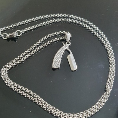 Colar prateado com pendente de navalha sobre superfície preta