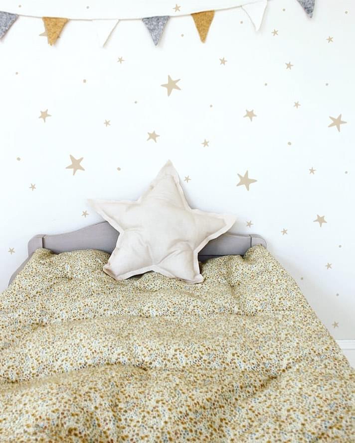 Cama infantil com edredão floral, almofada estrela e decoração de parede com estrelas douradas