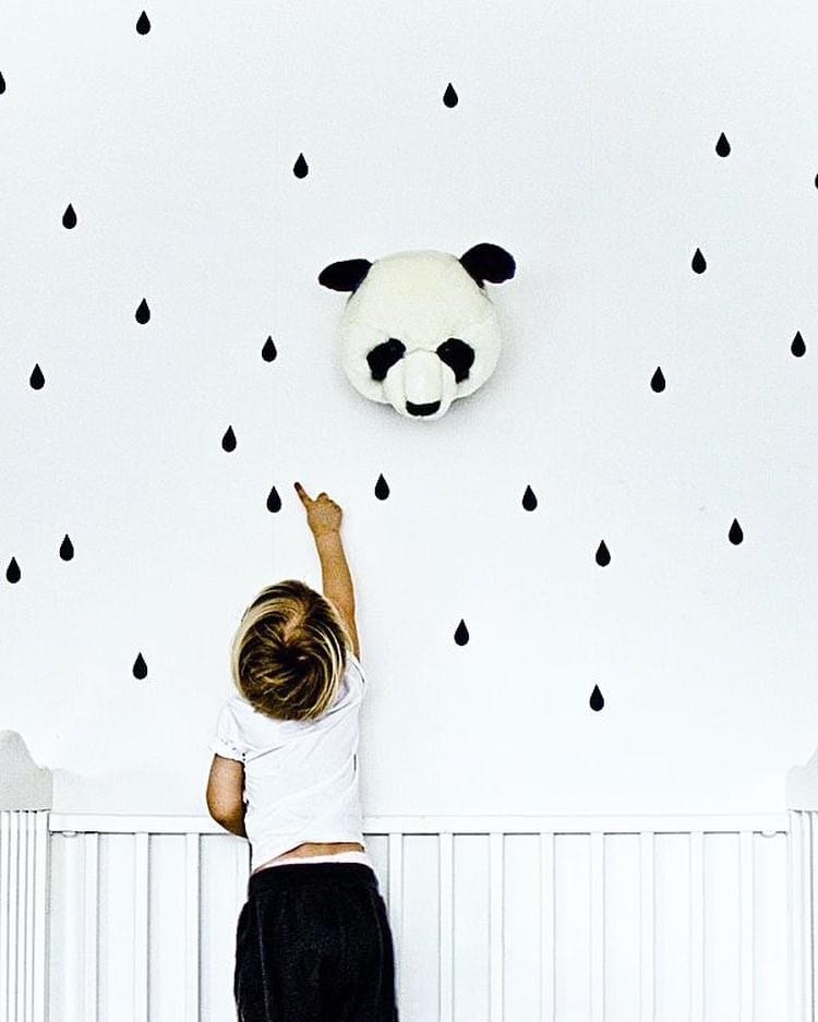 Cabeça de panda em tecido na parede branca com desenhos de gotas pretas e criança a apontar