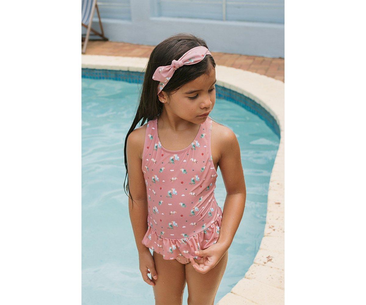 Menina com fato de banho rosa floral e faixa de cabelo rosa junto à piscina